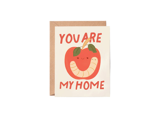 Greeting card with a worm and apple illustration and text 'You are my home' on a white background