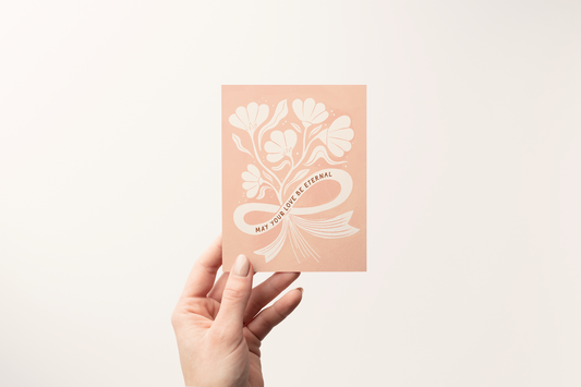 Hand holding a pink card with floral design and text on a light gray background