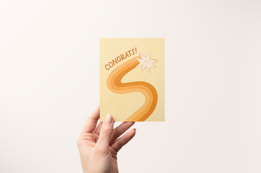 Hand holding a card with 'Congrats!' and a star and snake design on a light background