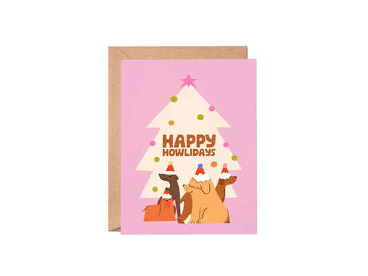 Greeting card with a cartoon dogs under a Christmas tree and 'Happy Howlidays' text on a pink background.